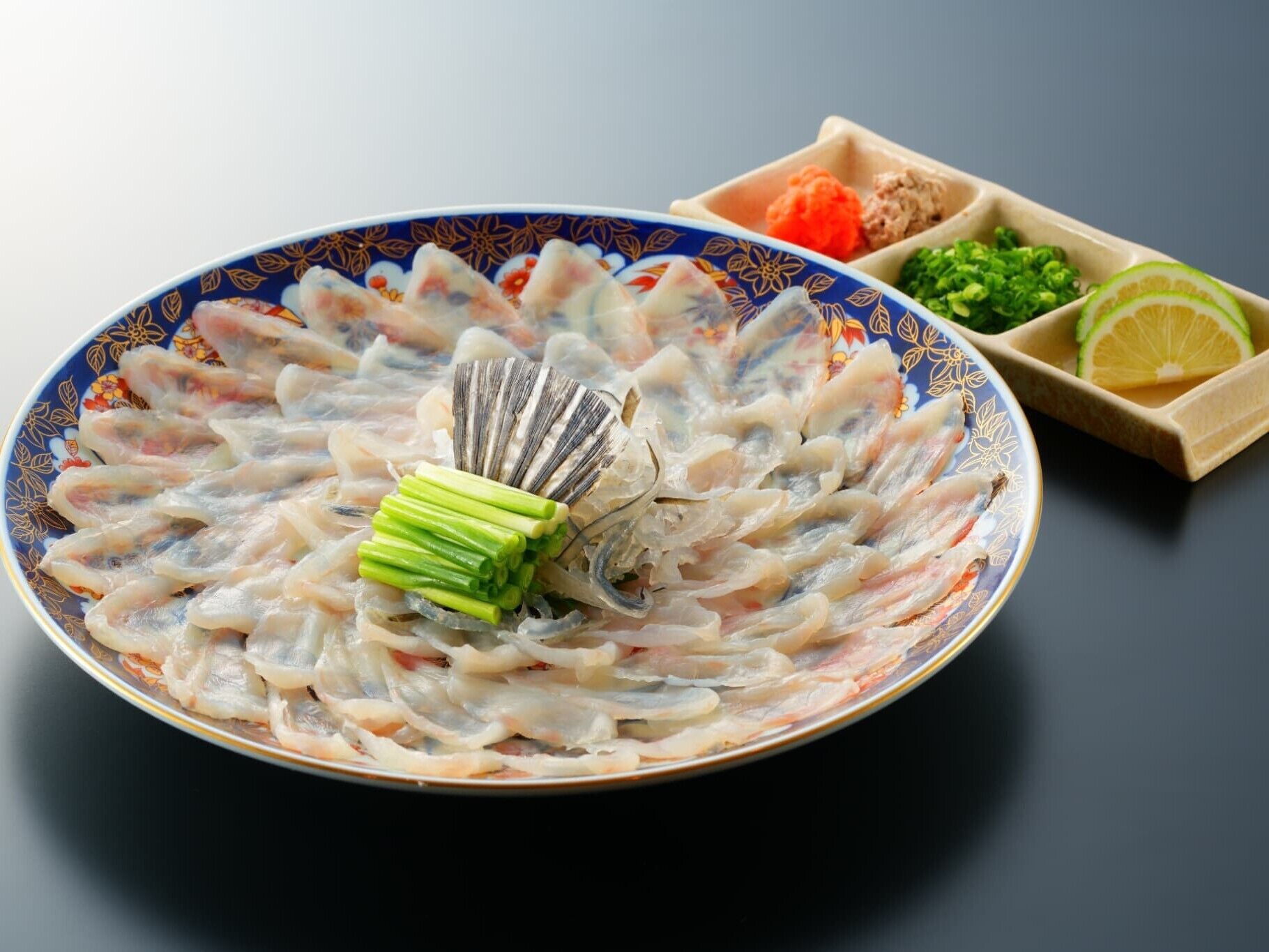 Eine Platte mit Sushi, einem verzierten Fächer, Frühlingszwiebeln und einer Beilage eingelegtes Gemüse.