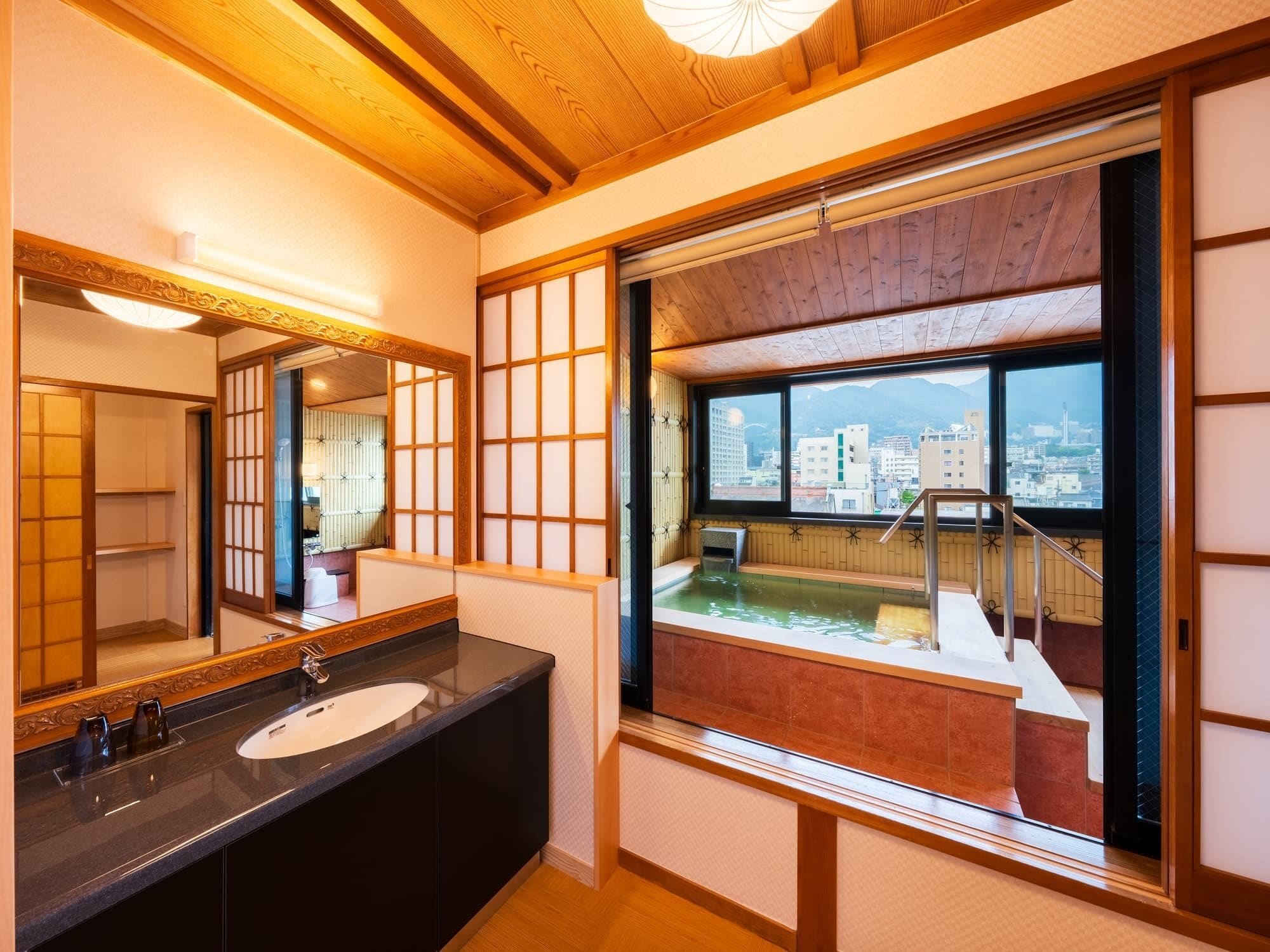 A modern bathroom with a large mirror, a sink, and a view of a cityscape through a large window.