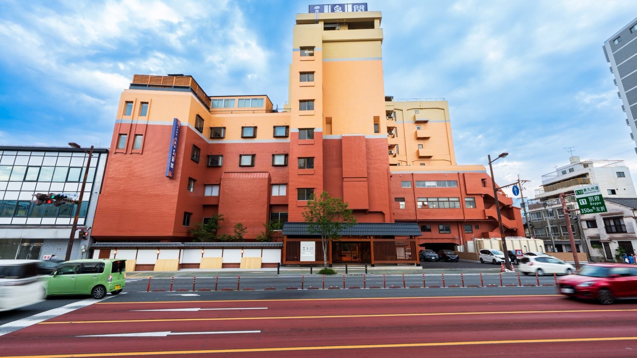A multi-story hotel with a prominent orange and beige facade, a visible entrance, and a street in front with cars and a bike lane.