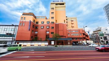A multi-story hotel with a prominent orange and beige facade, a visible entrance, and a street in front with cars and a bike lane.
