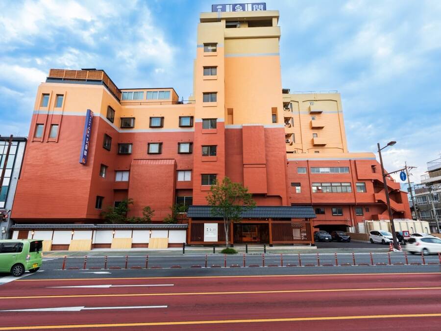 A multi-story hotel with a prominent orange and beige facade, a visible entrance, and a street in front with cars and a bike lane.