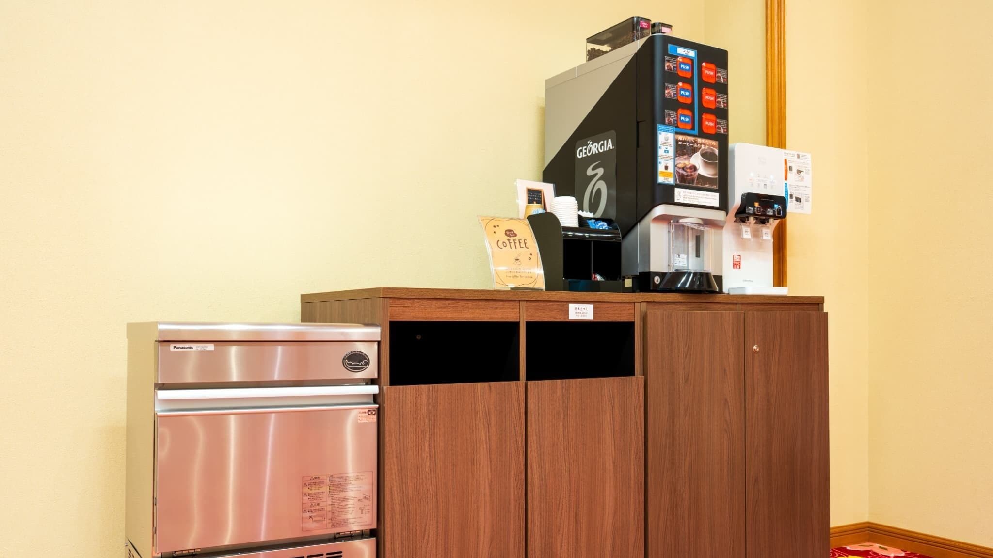 A kitchenette with a stainless steel refrigerator, a coffee machine, and a wooden cabinet.