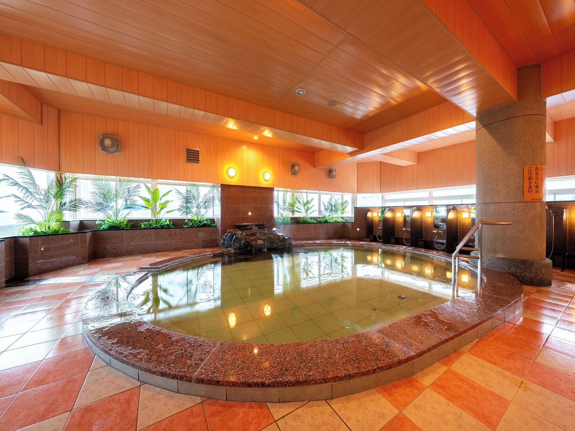 Una amplia piscina cubierta con borde de piedra, rodeada de paredes de madera y suelo de baldosas.