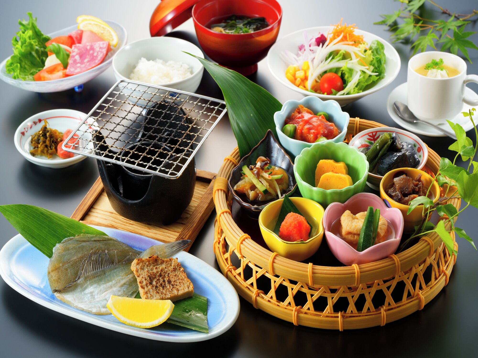 A variety of dishes including fish, rice, and vegetables, arranged on a table with a portable grill.