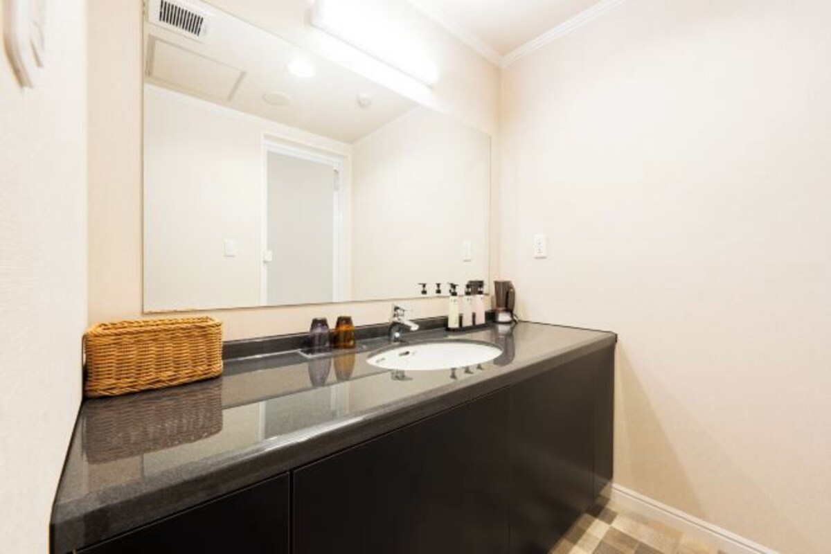 Un baño moderno con encimera negra, lavamanos blanco y un espejo grande.