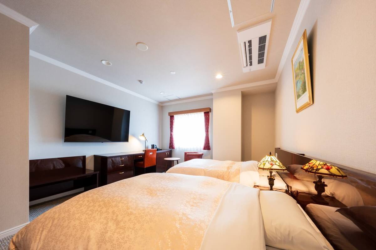 Ett hotellrum med två sängar, ett skrivbord, en tv och ett fönster med gardiner.