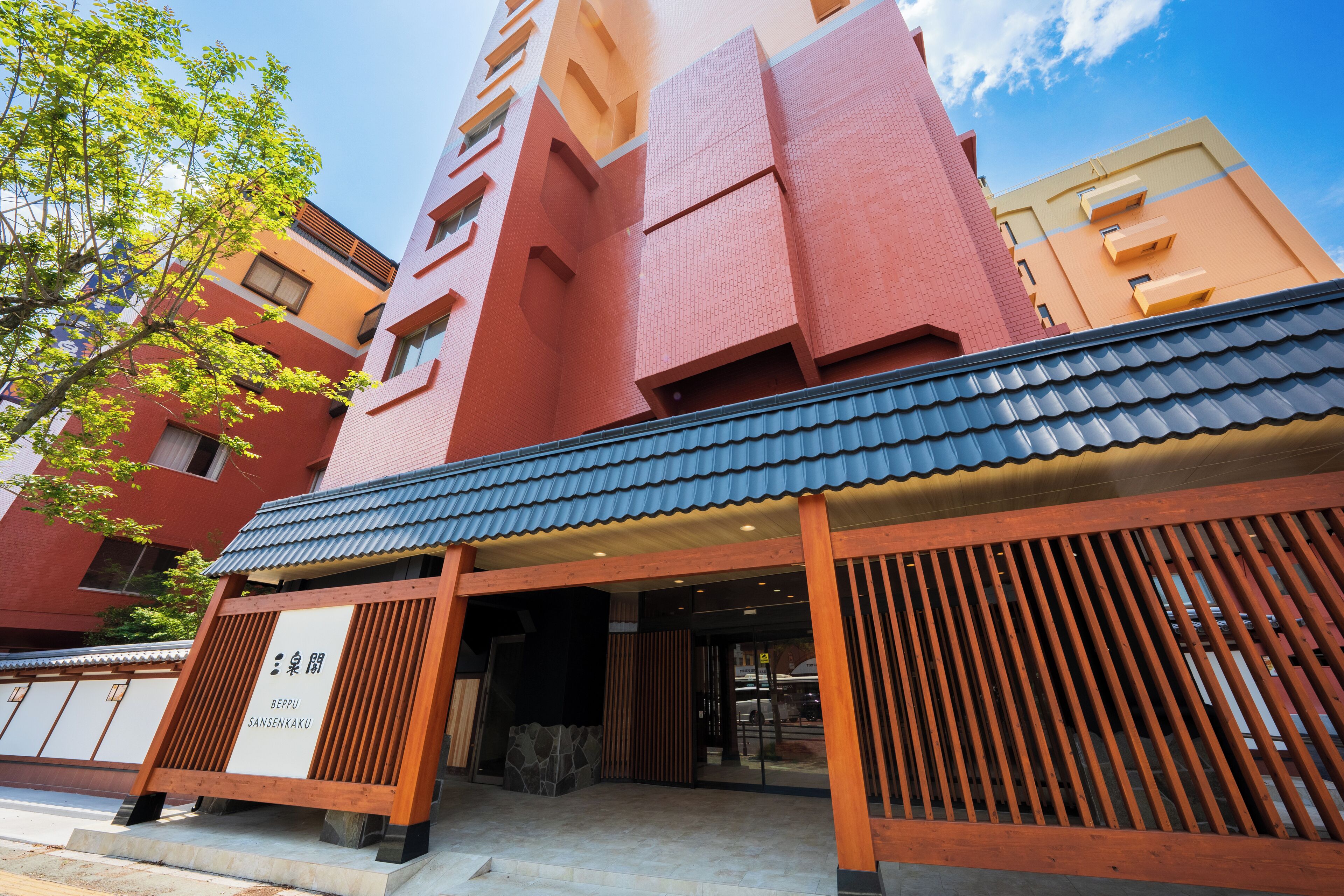 A multi-story building with a red and beige facade, wooden entrance with a sign, and a tiled roof.