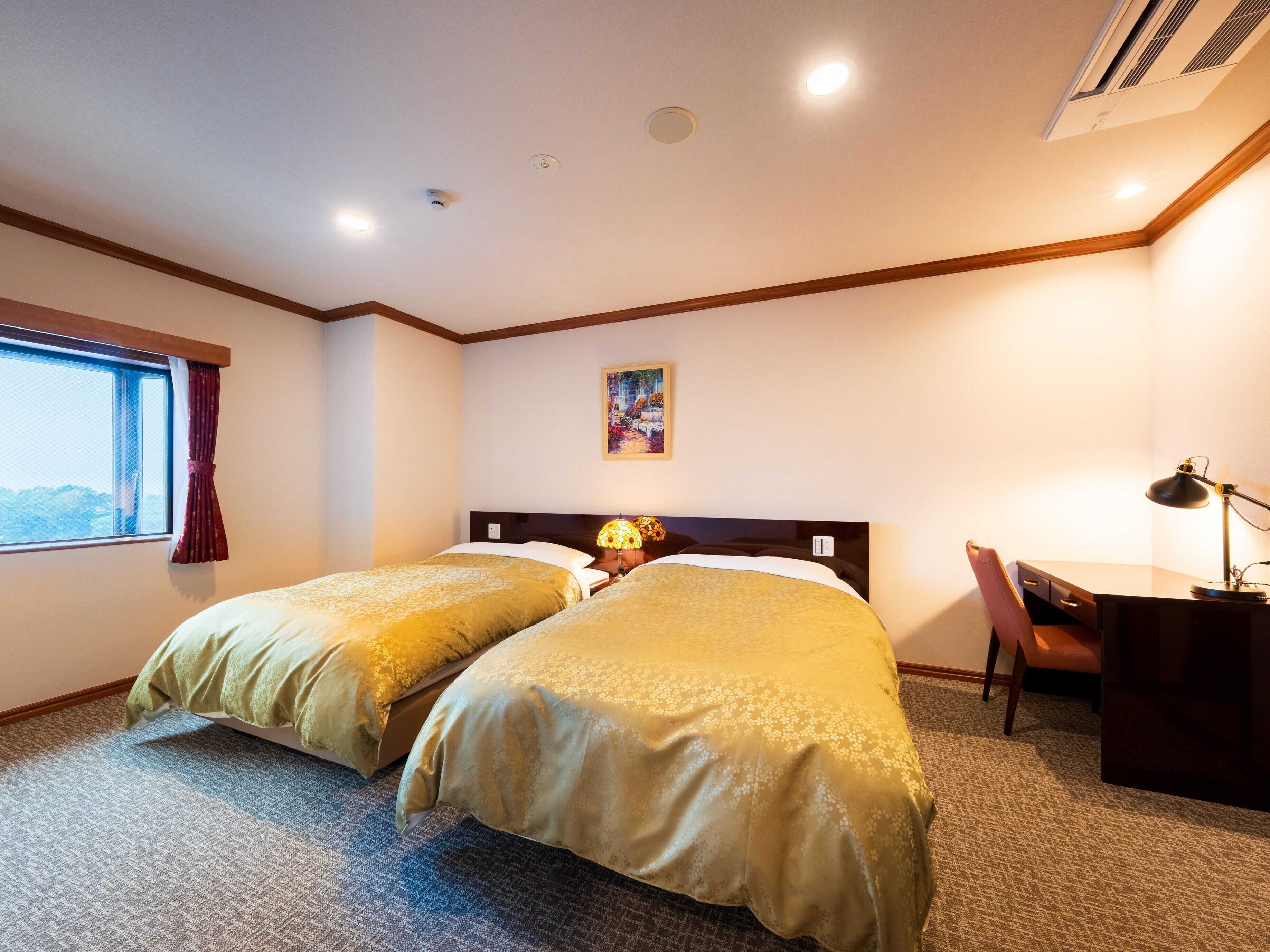 A hotel room with two beds, a desk, a chair, a window with curtains, and a painting on the wall.