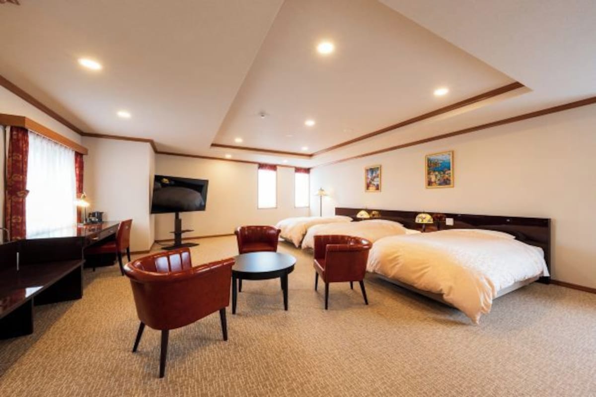 A hotel room with a large bed, a desk with a chair, a TV, and a small table.