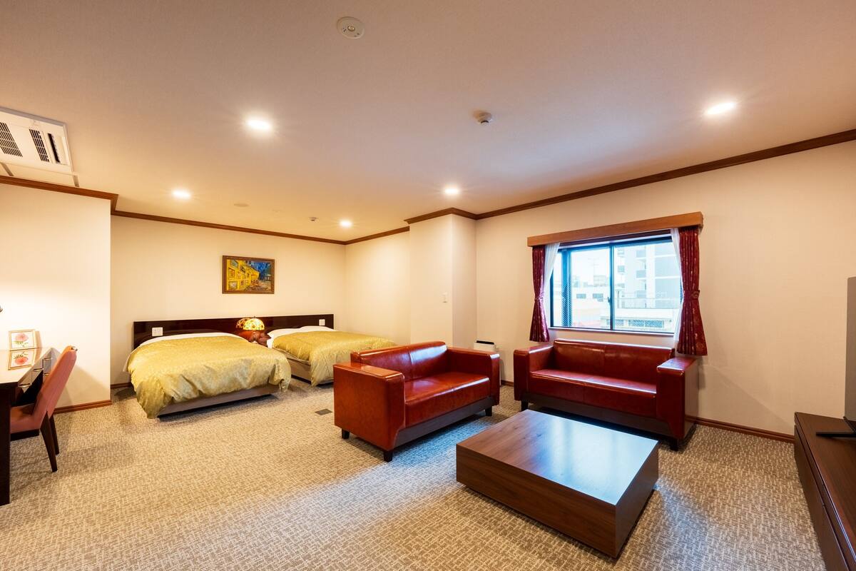 Ett hotellrum med två sängar, en röd soffa, ett träbord och ett fönster med gardiner.