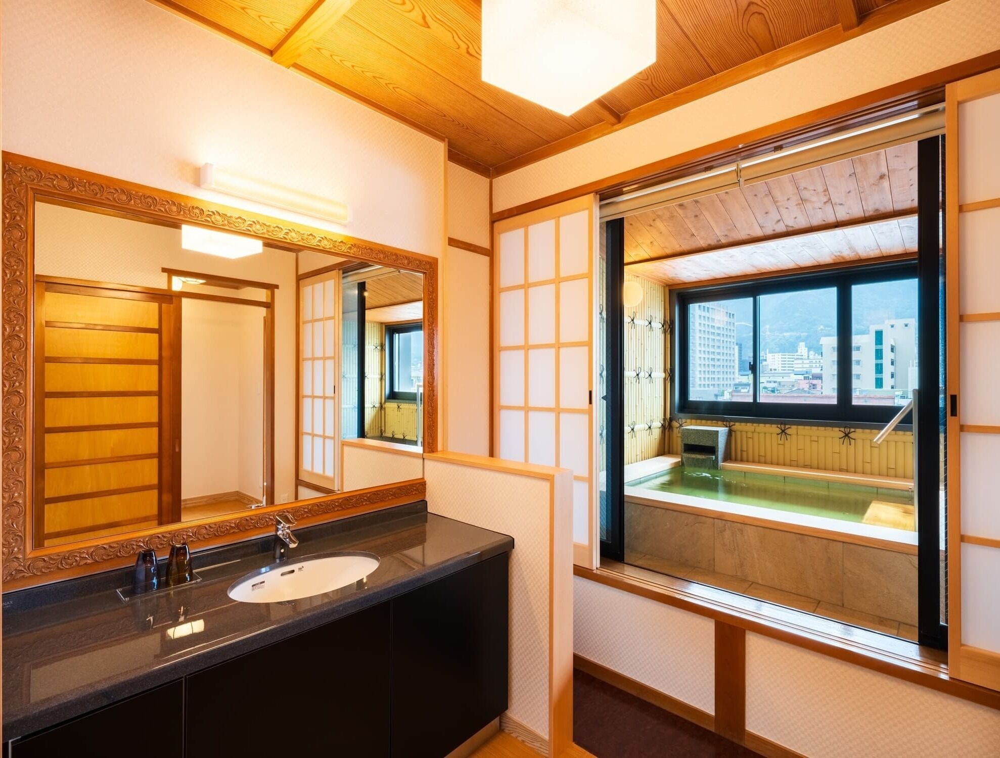 A modern bathroom with a large mirror, a sink, and a window with a view of buildings.
