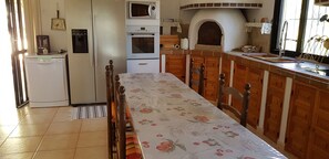 Een keuken met een eettafel, houten kastjes, een inbouwoven, een magnetron en een spoelbak.