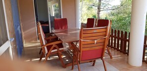 Een houten eettafel met stoelen, een glazen deur die naar een kamer leidt, en uitzicht op groen buiten.