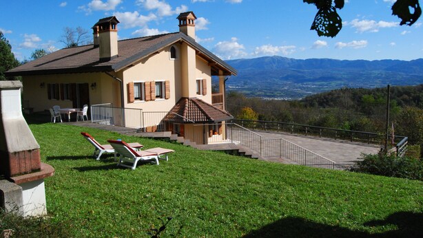 Une maison avec un balcon, une pelouse avec deux chaises longues et une vue sur les montagnes.