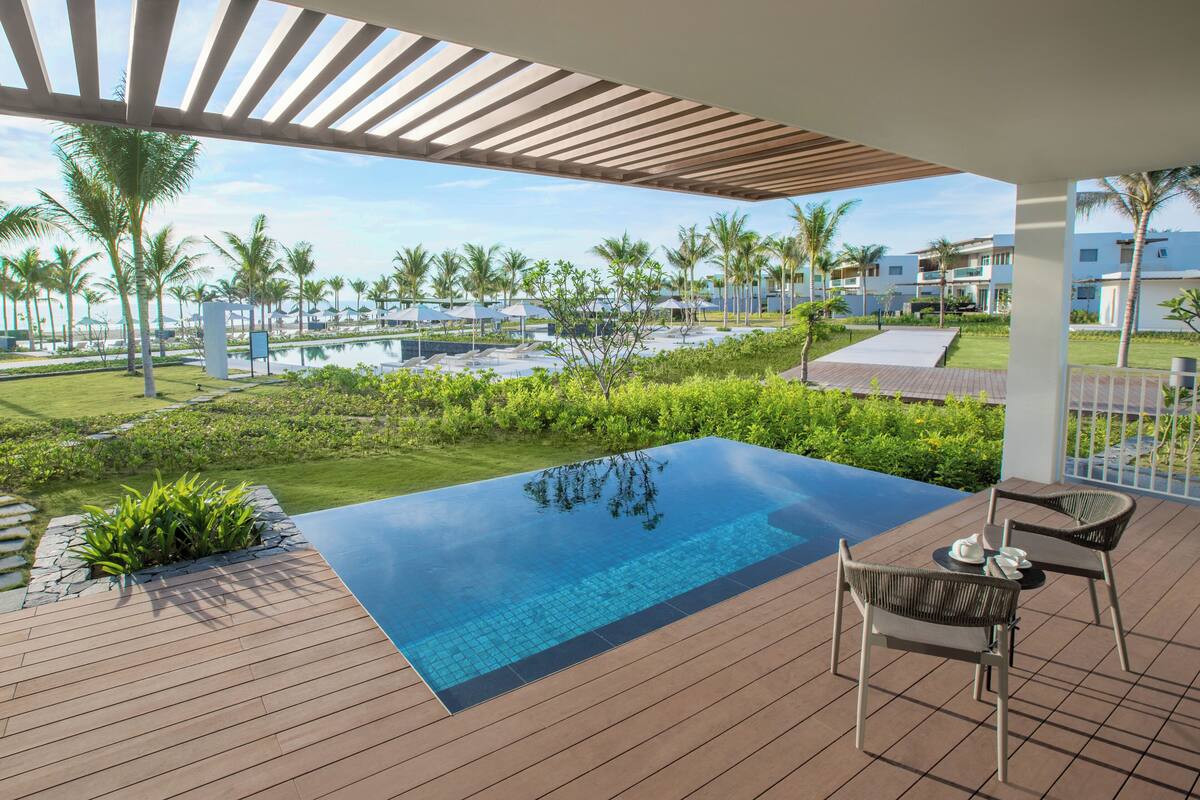 A rooftop infinity pool with a wooden deck, surrounded by lush greenery and palm trees.