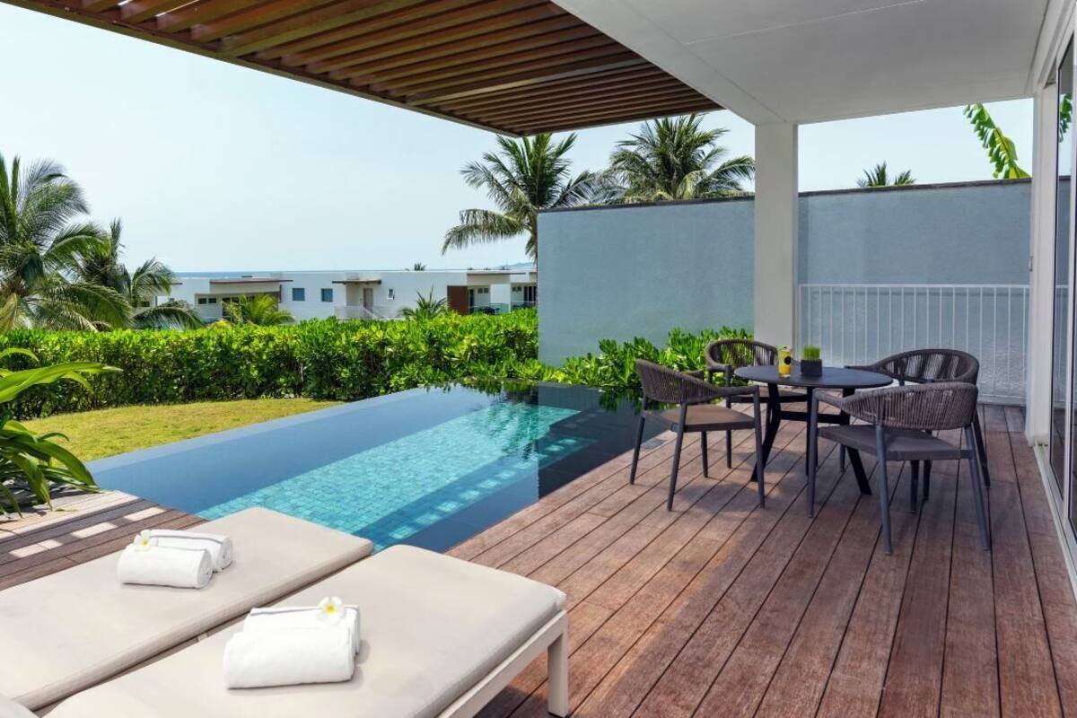 An infinity pool with a wooden deck, lounge chairs, and a table with chairs.