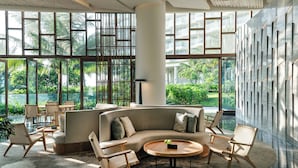 Un salon spacieux et moderne, doté d’un canapé incurvé, de chaises en bois et d’une table basse ronde. De grandes fenêtres offrent une vue sur la verdure environnante.