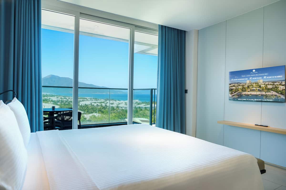 A hotel room with a large bed, a view of the sea, and a poster on the wall.