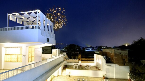 Terraço no telhado com área de estar externa e vista de fogos de artifício ao fundo.