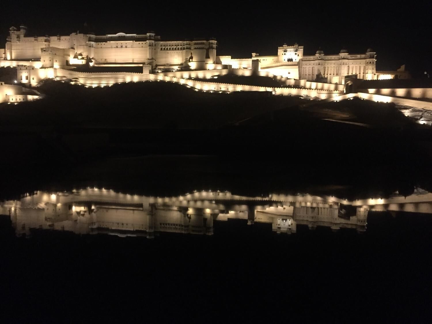 A large, illuminated fortress-like structure with a moat, reflecting its architecture in the water.