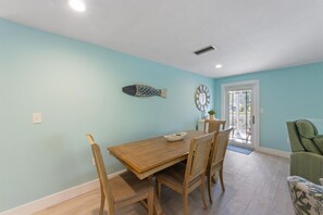 Un coin repas avec une table et des chaises en bois, un motif décoratif représentant des poissons sur le mur, et une vue à travers une porte vitrée.