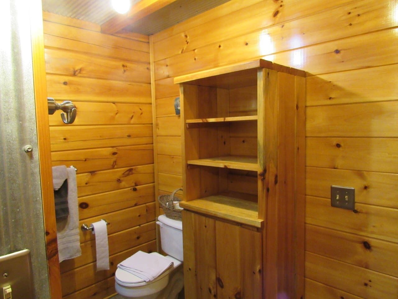 A wooden cabin bathroom with a toilet, a sink, and a shelf unit.