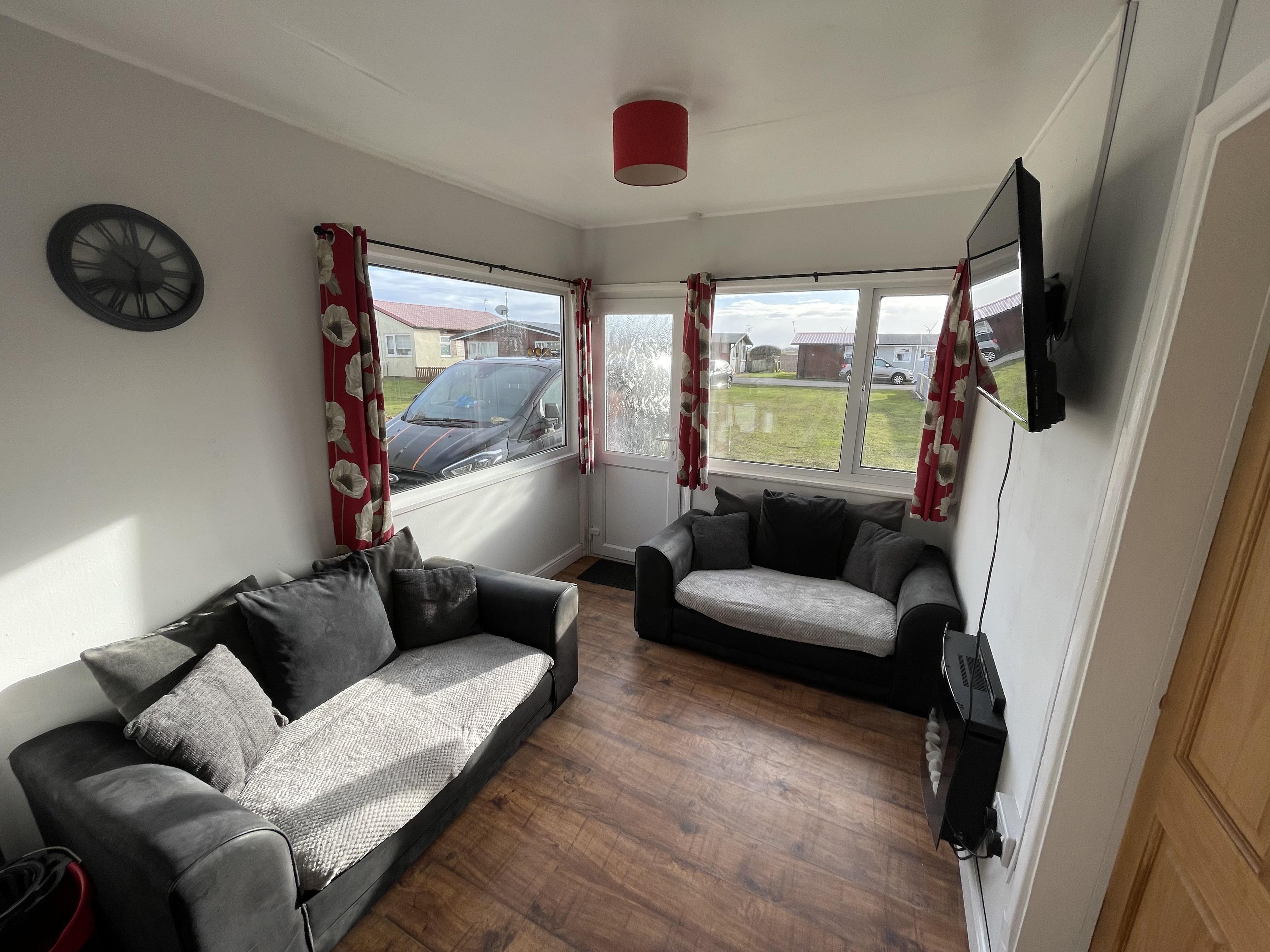 A living room with a sofa, a smaller chair, a flat-screen TV, and a clock on the wall.