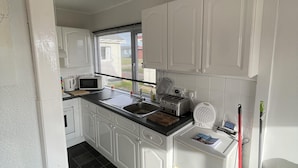 A compact kitchen with white cabinets, a sink, a microwave, and a toaster. - Captivating 2-bed Chalet (Bridlington)