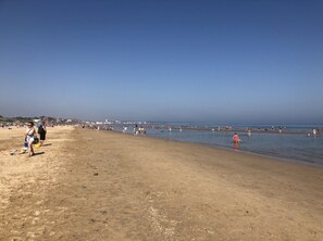 Una amplia playa de arena con gente caminando y nadando.