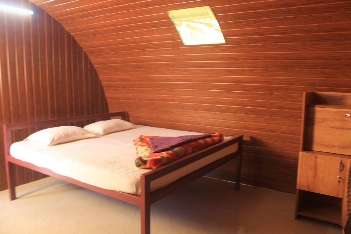 A single bed with a wooden headboard, a small cabinet, and a slanted ceiling.