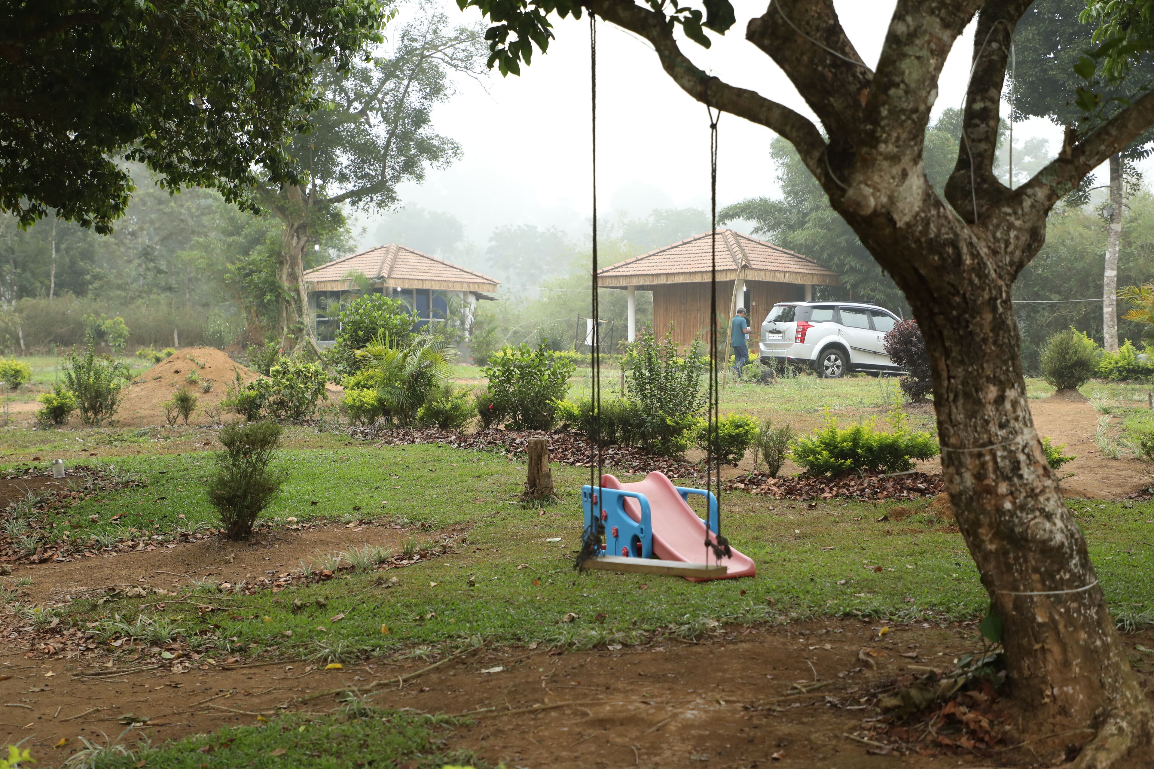 A park with a swing set, a white car, and a building with a tiled roof.
