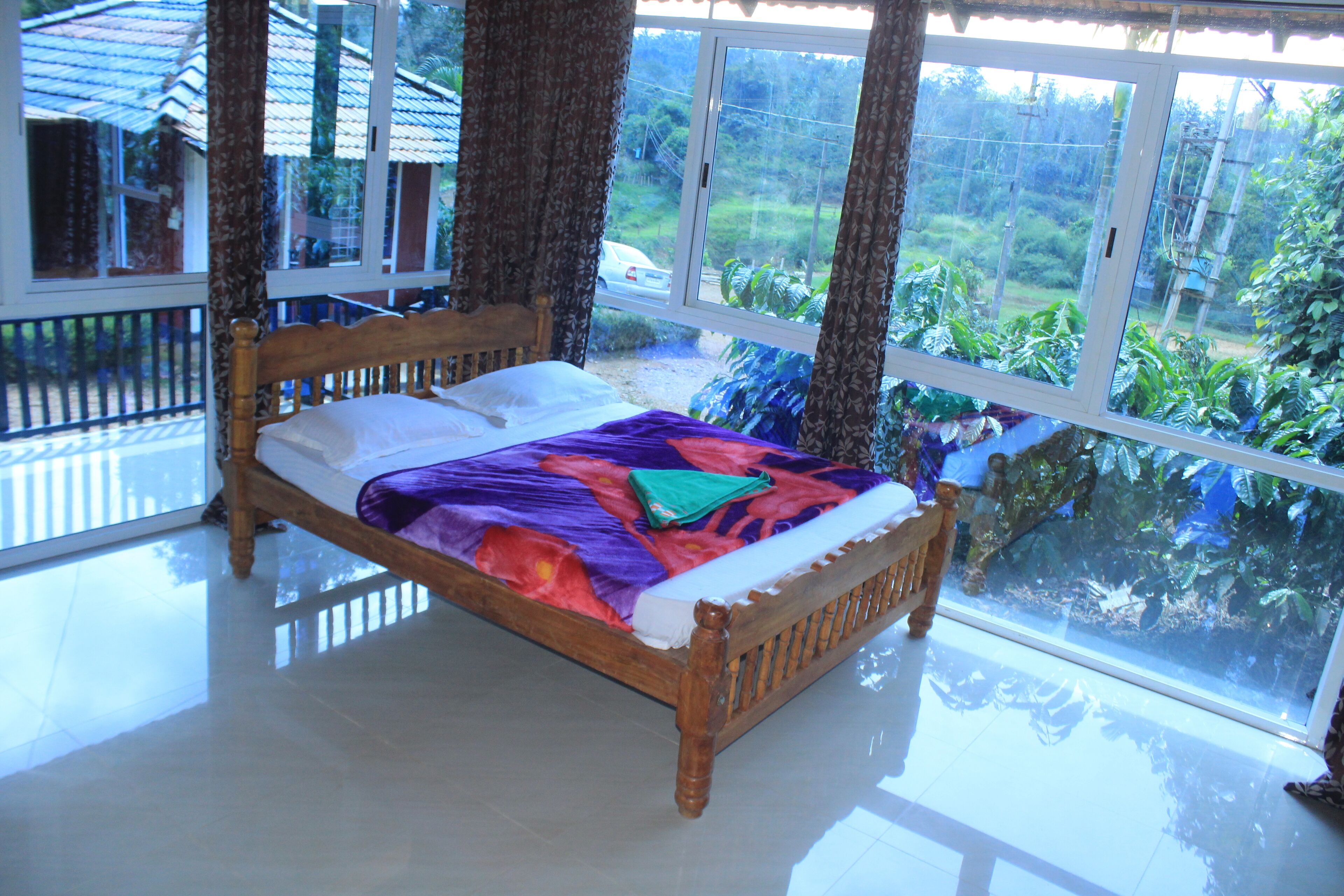 Una cama con estructura de madera y una colcha colorida, ubicada en una habitación con ventanas amplias que dan a vistas de vegetación.