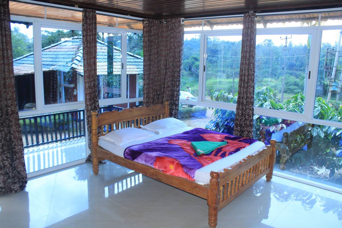 A wooden bed with a colorful blanket in a room with large windows and curtains.