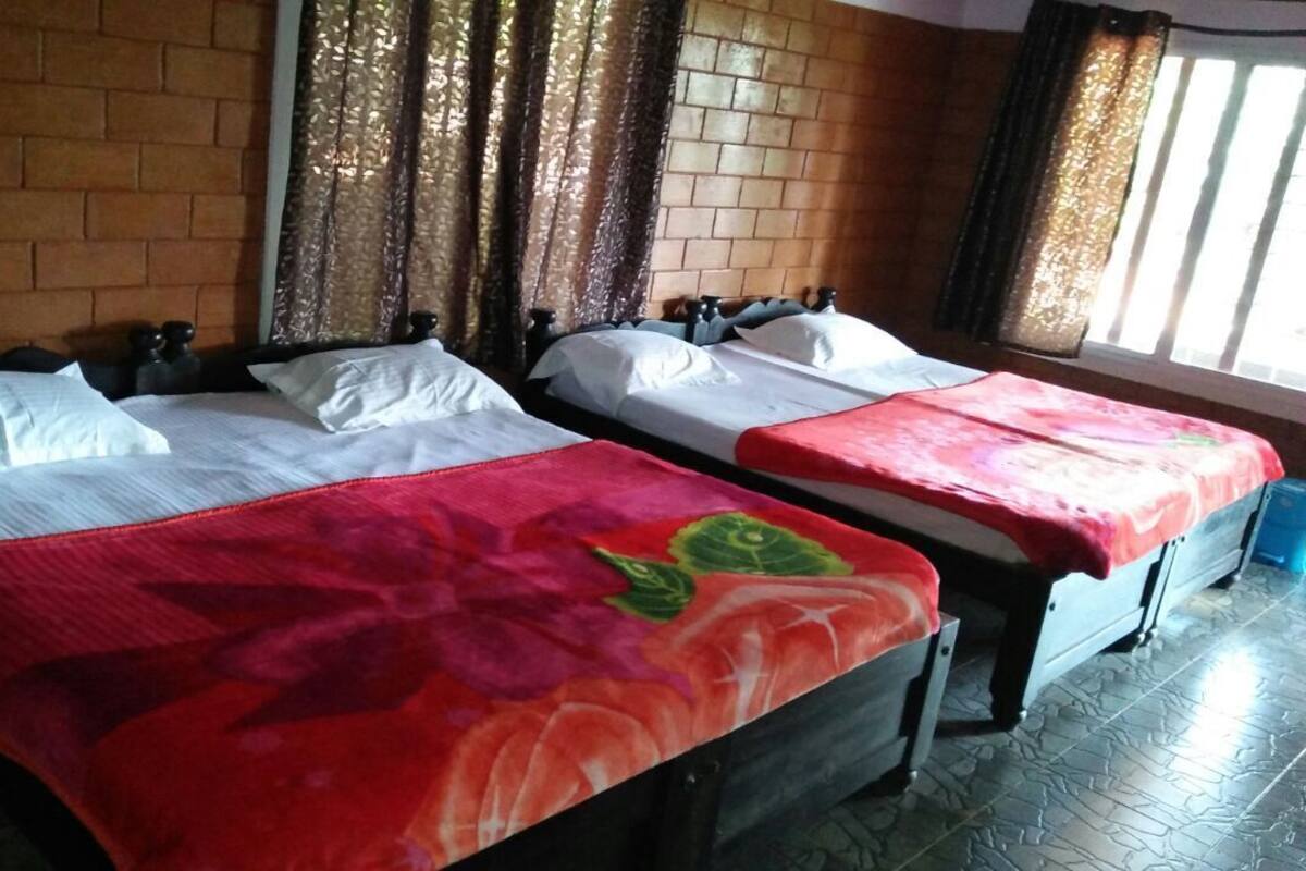 A room with two beds, each with a red floral bedspread, a brick wall, and curtains.
