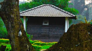 A traditional wooden building with a tiled roof, surrounded by lush greenery. - Muccole Stay (Madikeri)