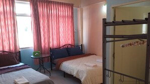 A room with two beds, a small table, and a window with curtains. - OK Home Hostel (Bangkok)