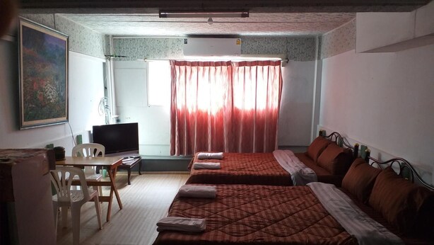 A hotel room with two beds, a desk, a television, and a window with curtains. - OK Home Hostel (Bangkok)