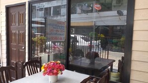 A dining area with a table and chairs, a window with a view of the street, and a sign advertising a sale. - OK Home Hostel (Bangkok)