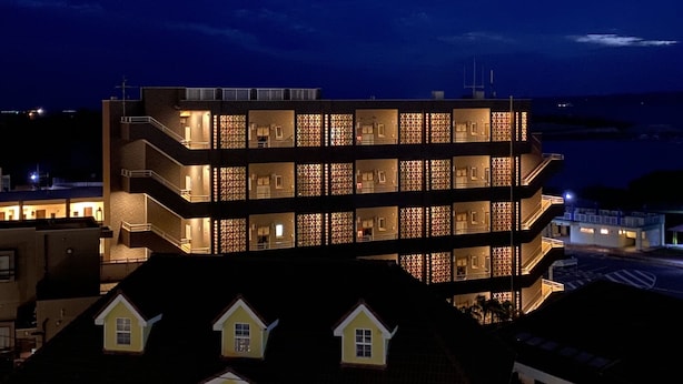 A multi-story building with illuminated windows and balconies, located near a body of water. - Ocean Front Miyakojima (Miyakojima)