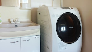 A compact, white laundry room with a washing machine and a sink. - Ocean Front Miyakojima (Miyakojima)