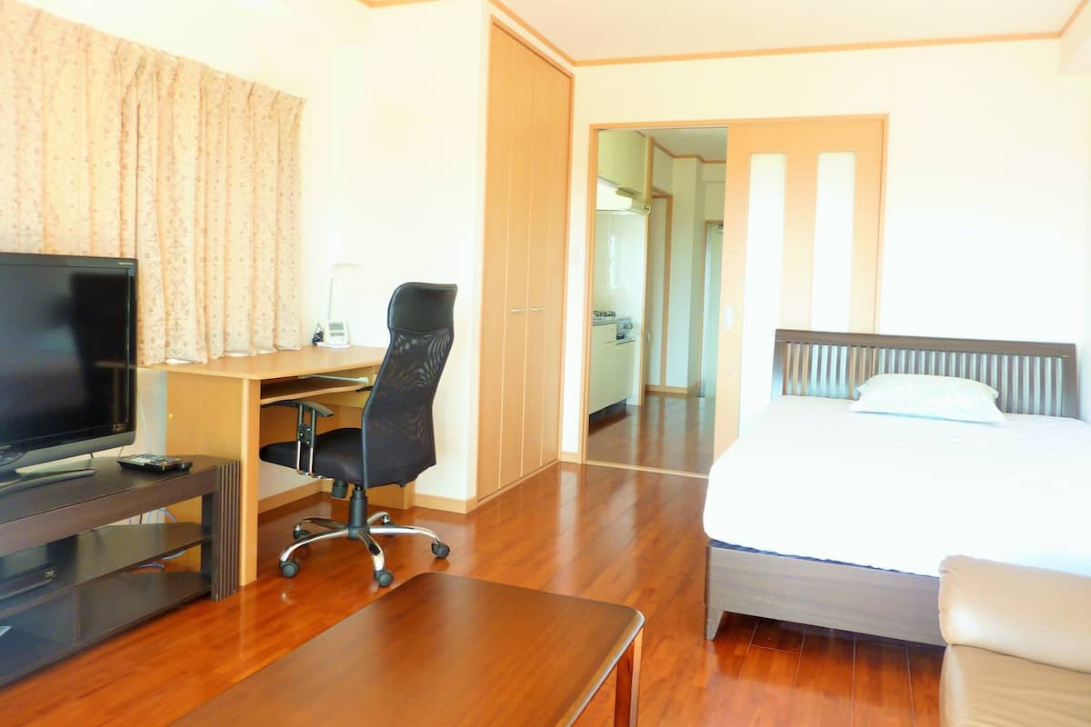 Une chambre d’hôtel avec un lit, un bureau et une chaise, une télévision et une salle de bain visible à travers une porte ouverte.