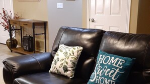 A black leather sofa with two decorative pillows, a patterned rug, and a wall with a wine bottle artwork. - Spacious Two-Bedroom Suite in Salt Lake Valley (West Jordan)
