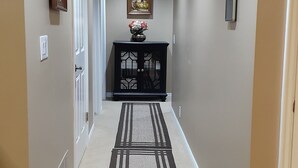 A hallway with beige walls, a patterned rug, a black console table with a vase, and a painting on the wall. - Spacious Two-Bedroom Suite in Salt Lake Valley (West Jordan)
