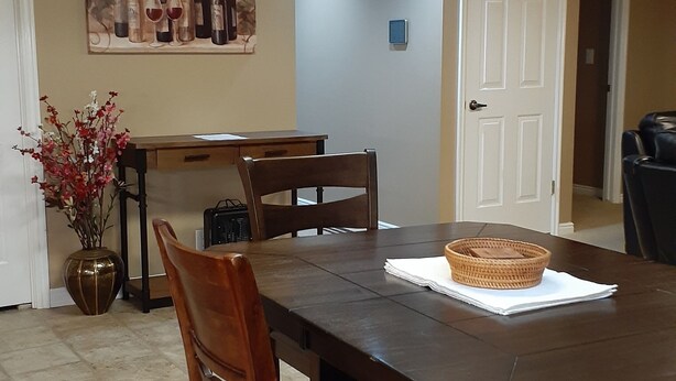 A dining room with a large wooden table, four chairs, a vase of flowers, and a painting on the wall. - Spacious Two-Bedroom Suite in Salt Lake Valley (West Jordan)