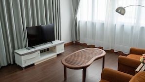 A modern living room with a flat-screen TV on a white console, a wooden coffee table, and orange armchairs. - FnF HOUSING (Hanoi)