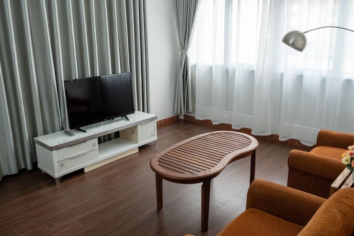 A modern living room with a flat-screen TV on a white console, a wooden coffee table, and orange armchairs.