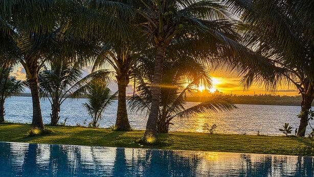 A pool with clear water, surrounded by palm trees and a sunset view. - Ashansa Lagoon Resort (Rekawa)