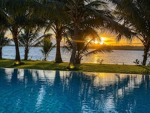 Una piscina con agua cristalina, rodeada de palmeras y vistas al atardecer.