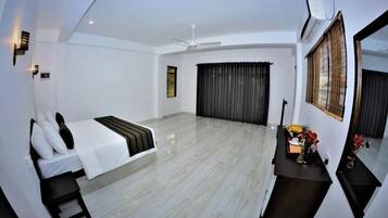 Amplia habitación de hotel con cama, escritorio, silla, ventana grande con cortinas, ventilador de techo y aire acondicionado.