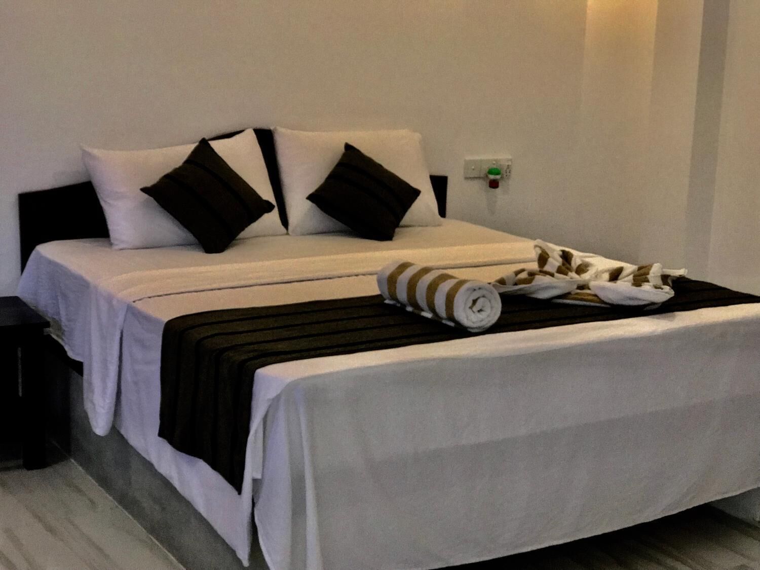 A neatly made bed with white and black bedding, a striped towel, and a small table beside it.
